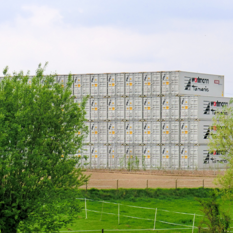 Gestapelte graue Container vor grüner Wiese und Bäumen – BOBE