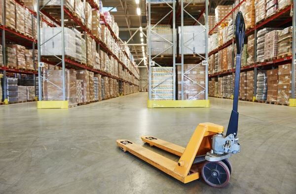 Ein gelber Hubwagen steht einsatzbereit in einem weiten Gang eines Hochregallagers – BOBE
