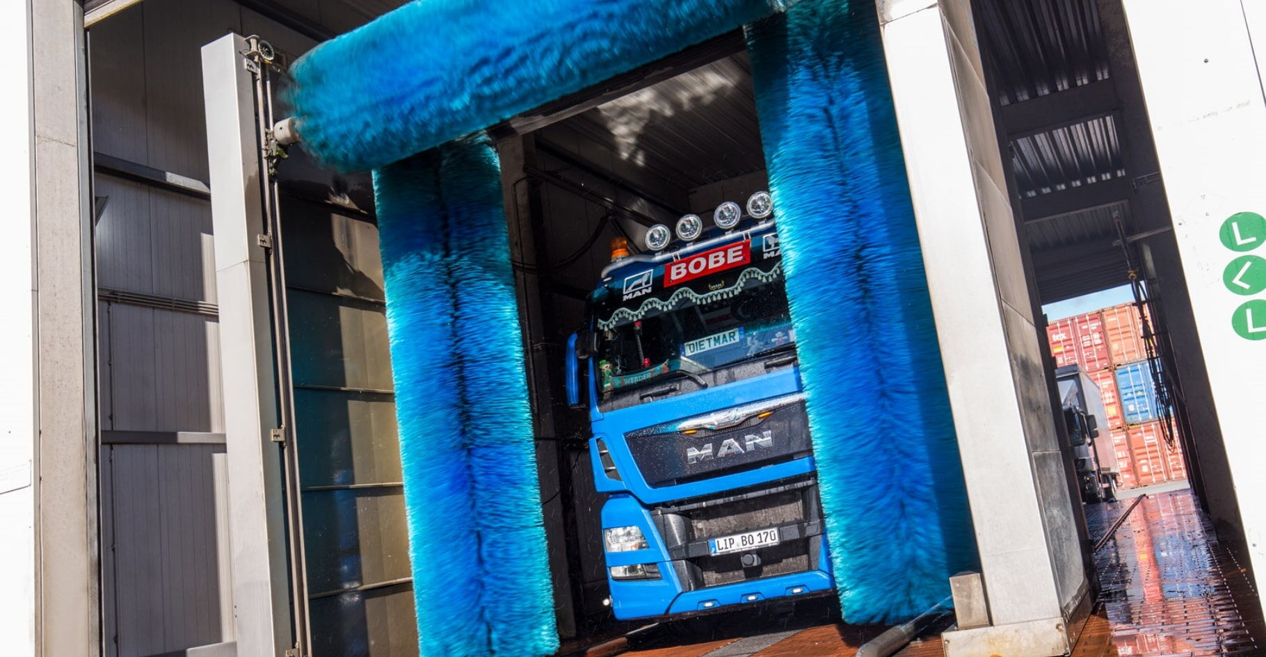Ein blauer LKW fährt durch eine Waschanlage mit großen blauen Bürsten – BOBE
