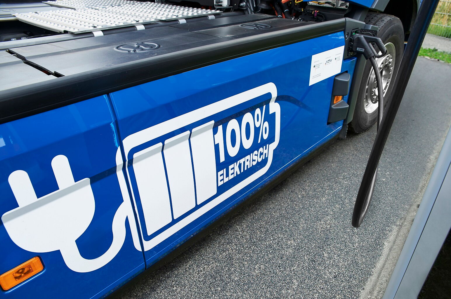 Seitenansicht eines blauen BOBE E-LKW mit großem Batterie-Symbol und eingestecktem Ladekabel – BOBE