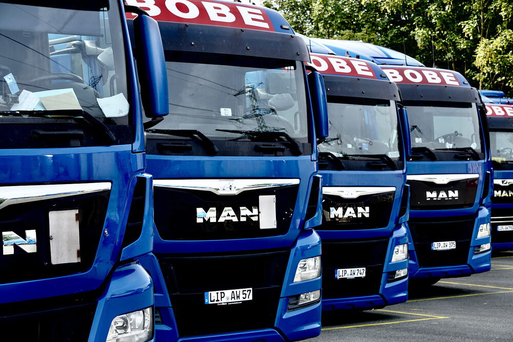 Mehrere blaue BOBE-Zugmaschinen der Marke MAN stehen in einer Reihe auf dem Betriebsgelände – BOBE