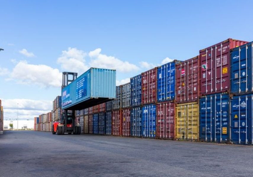 Ein Reachstacker hebt einen blauen BOBE-Container im Containerlager bei sonnigem Wetter