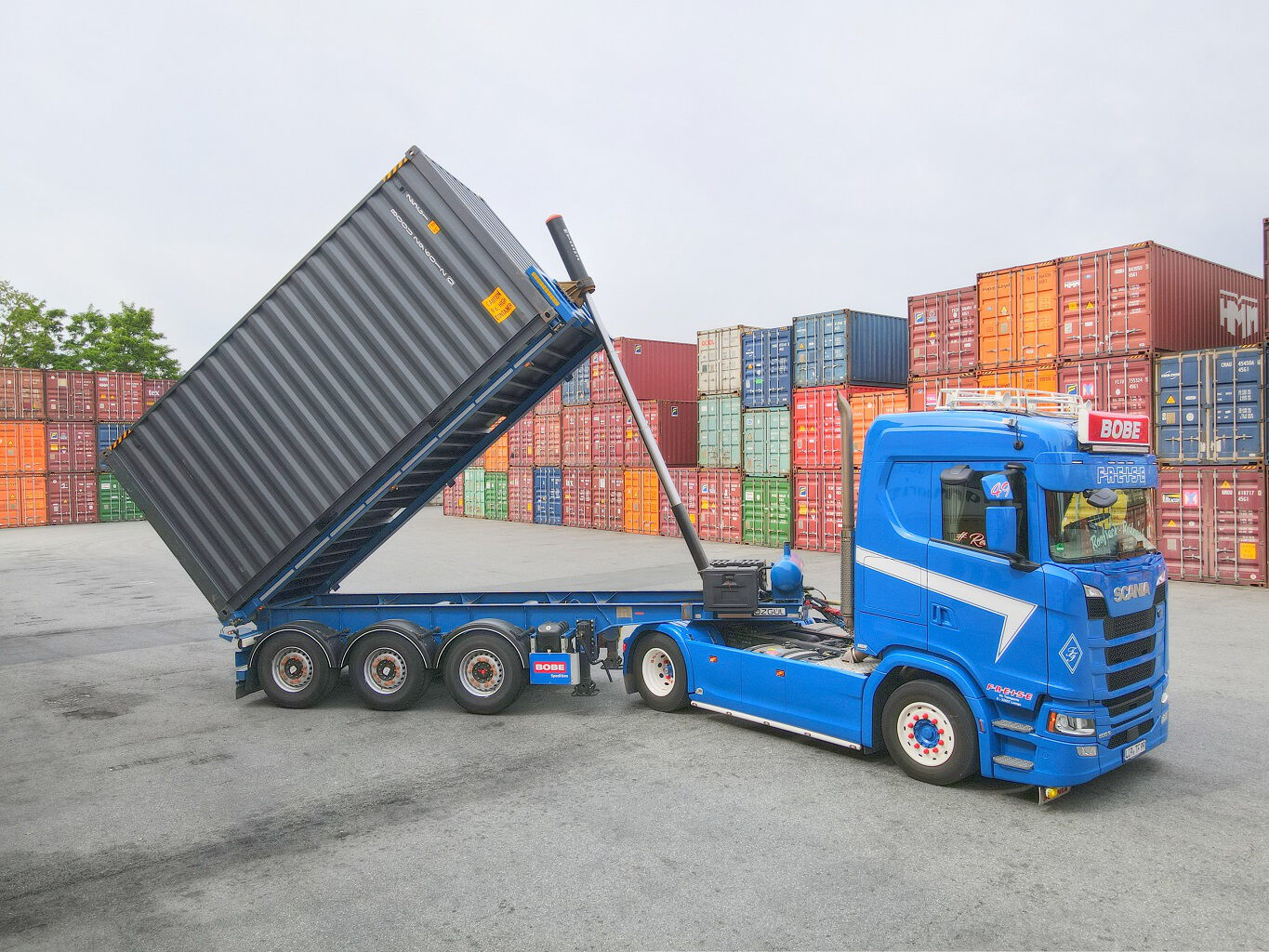 Ein blauer BOBE-LKW mit gekipptem Container-Auflieger zur Entladung von Schüttgut auf dem Terminalgelände – BOBE