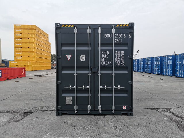 Rückansicht eines anthrazitfarbenen Containers im Depot mit gelben Containerstapeln im Hintergrund