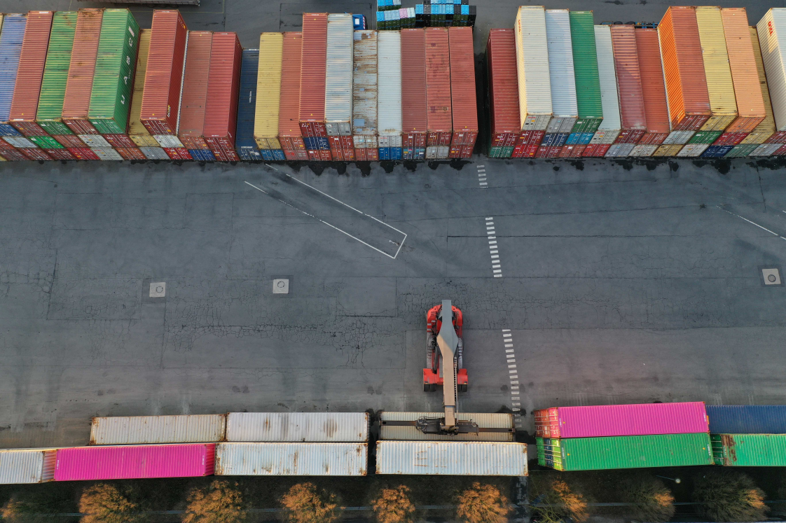Senkrechte Luftaufnahme von bunten Containerreihen und einem Arbeitsfahrzeug auf dem Firmengelände