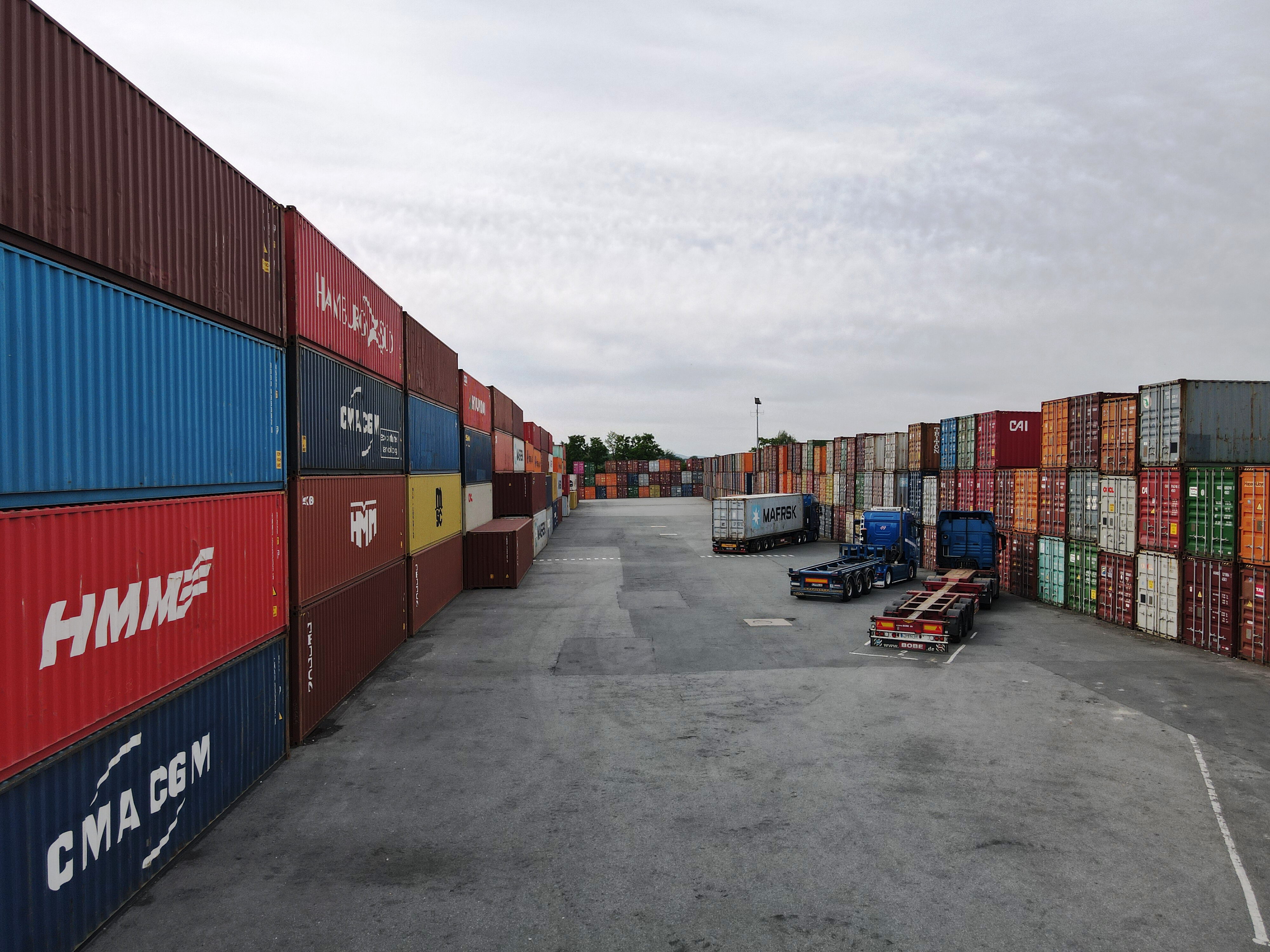 Weitwinkelaufnahme eines Terminals mit hoch gestapelten Seecontainern und rangierenden LKW-Fahrgestellen – BOBE