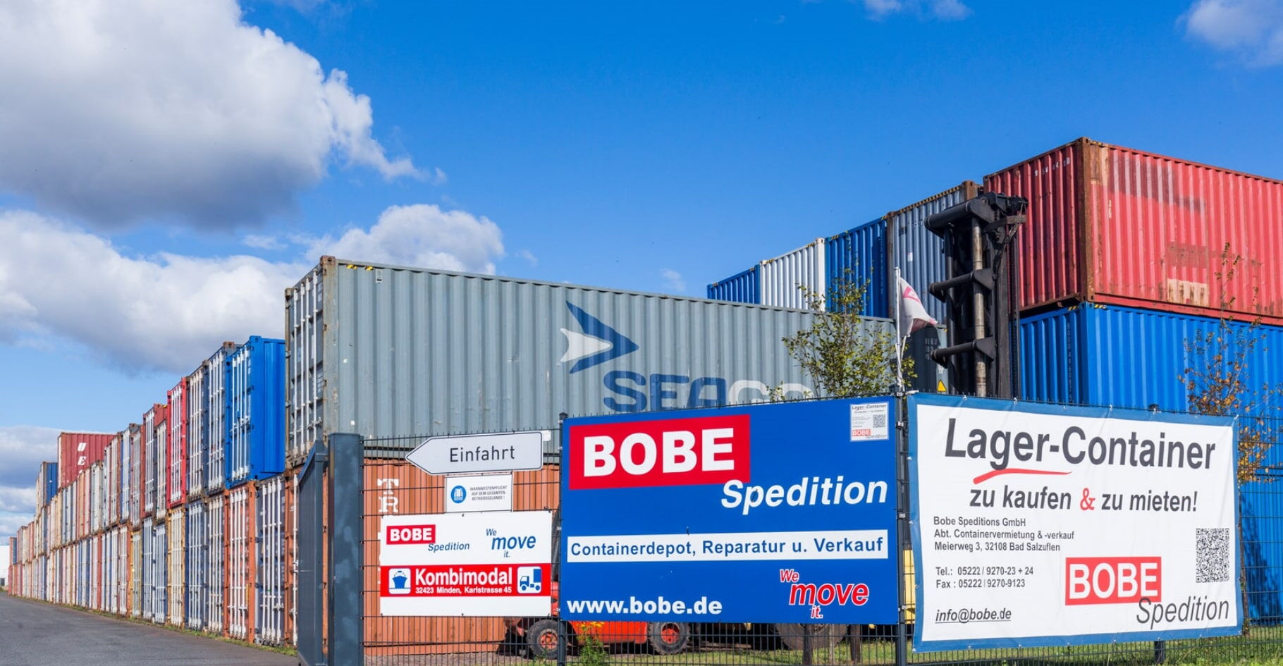 Einfahrt zum Betriebsgelände mit Informationsschildern vor hohen Containerstapeln – BOBE