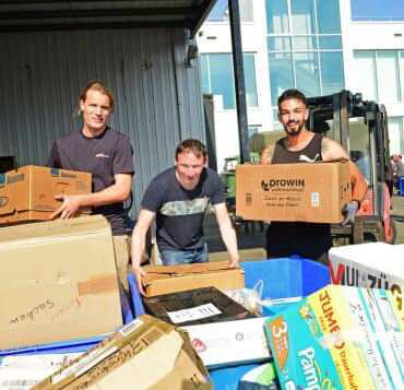 Drei Mitarbeiter sortieren Spendenkartons und Hilfsgüter vor BOBE Lagerhalle – BOBE