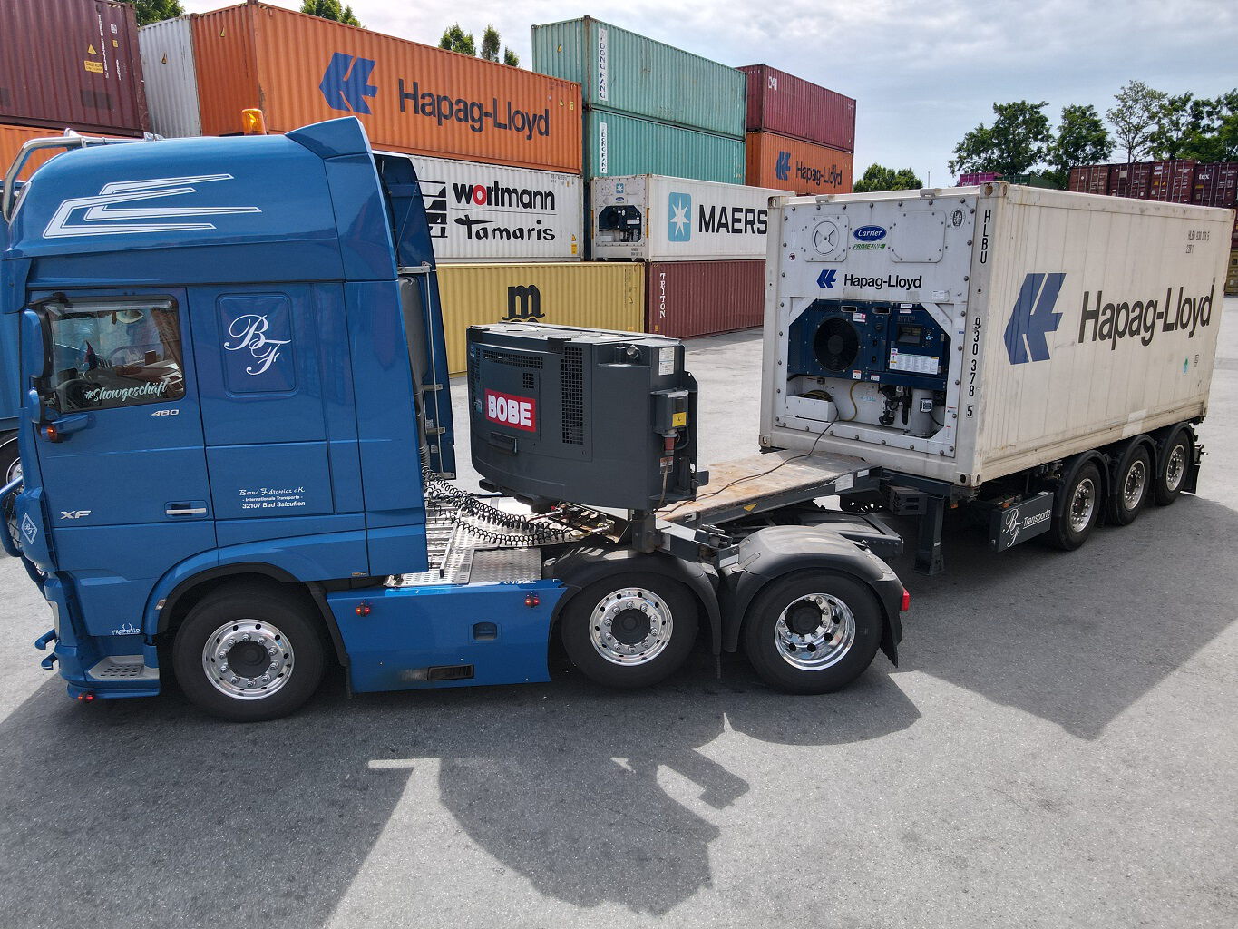 Blauer LKW mit angekoppeltem Kühlcontainer auf einem Containerdepot – BOBE