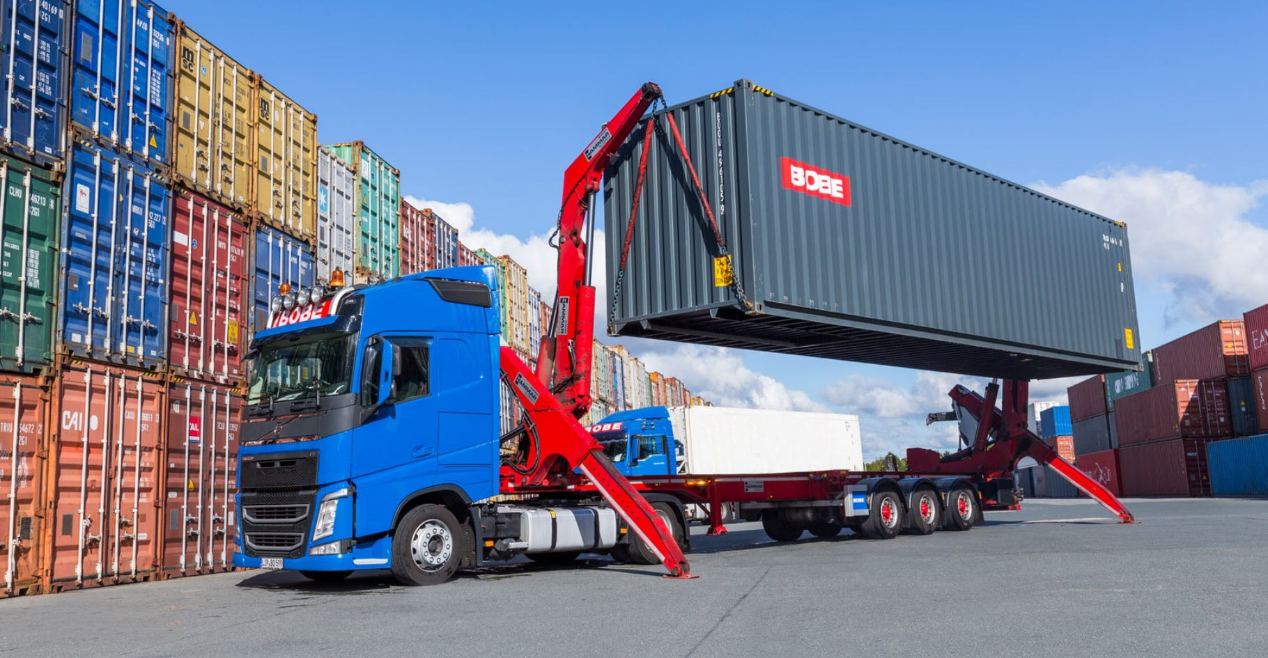 Ein blauer LKW hebt mit einem Seitenlader einen grauen Container an – BOBE