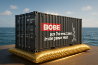 Schwarzer Seefracht-Container mit BOBE Logo auf einem goldenen Kissen vor Meereskulisse