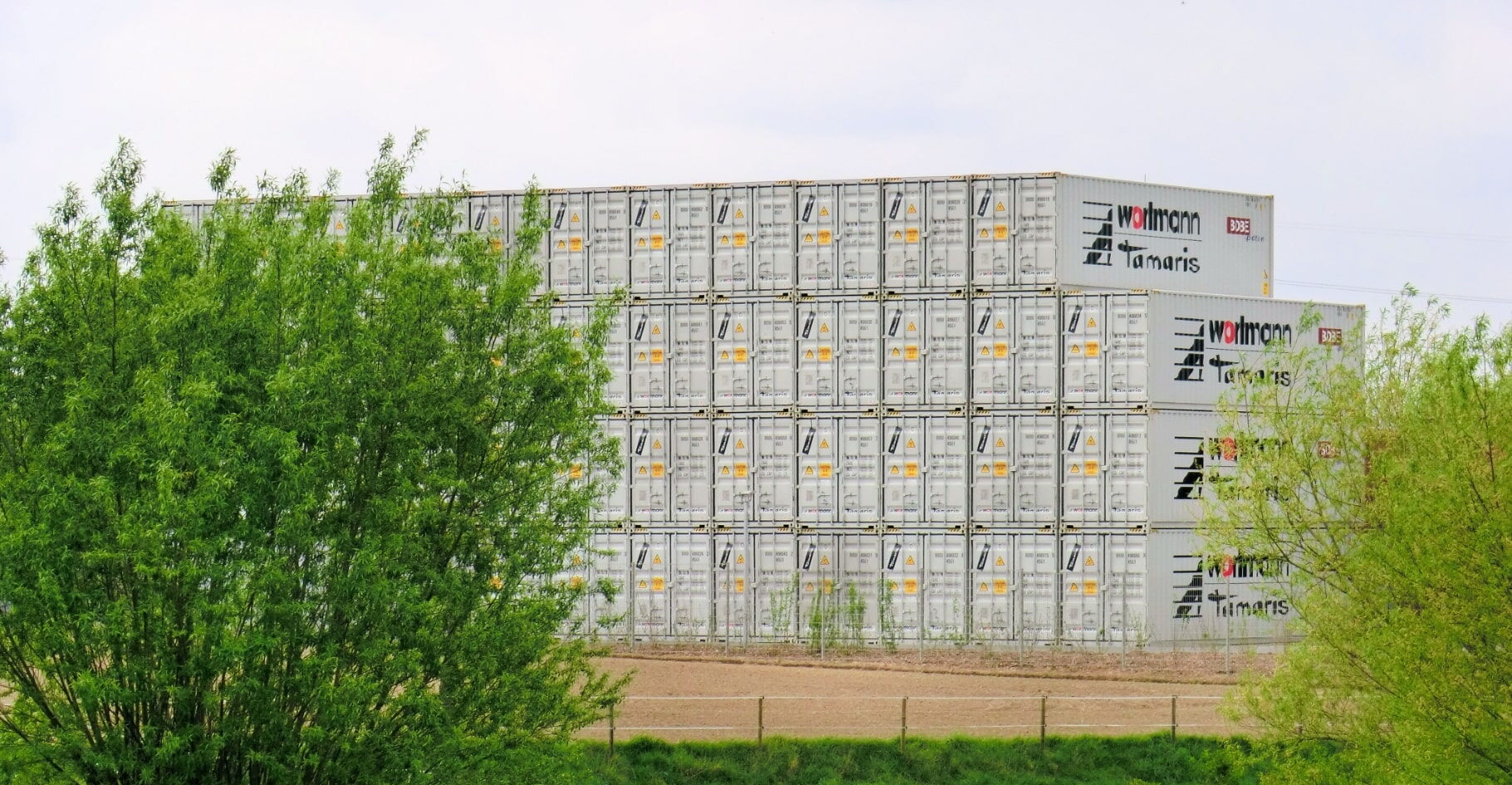 Mehrere Reihen weißer Container mit Logo-Aufdruck auf einem Lagerplatz im Grünen – BOBE